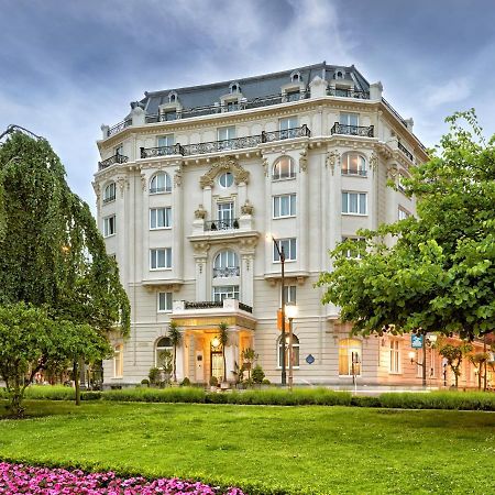 卡尔顿酒店 毕尔巴鄂 外观 照片 The photo depicts a beautiful, historic building, likely a hotel or a residence, featuring an elegant architectural style with white facade and ornate details. It is surrounded by a lush green lawn, trees, and colorful flower beds that enhance the ae