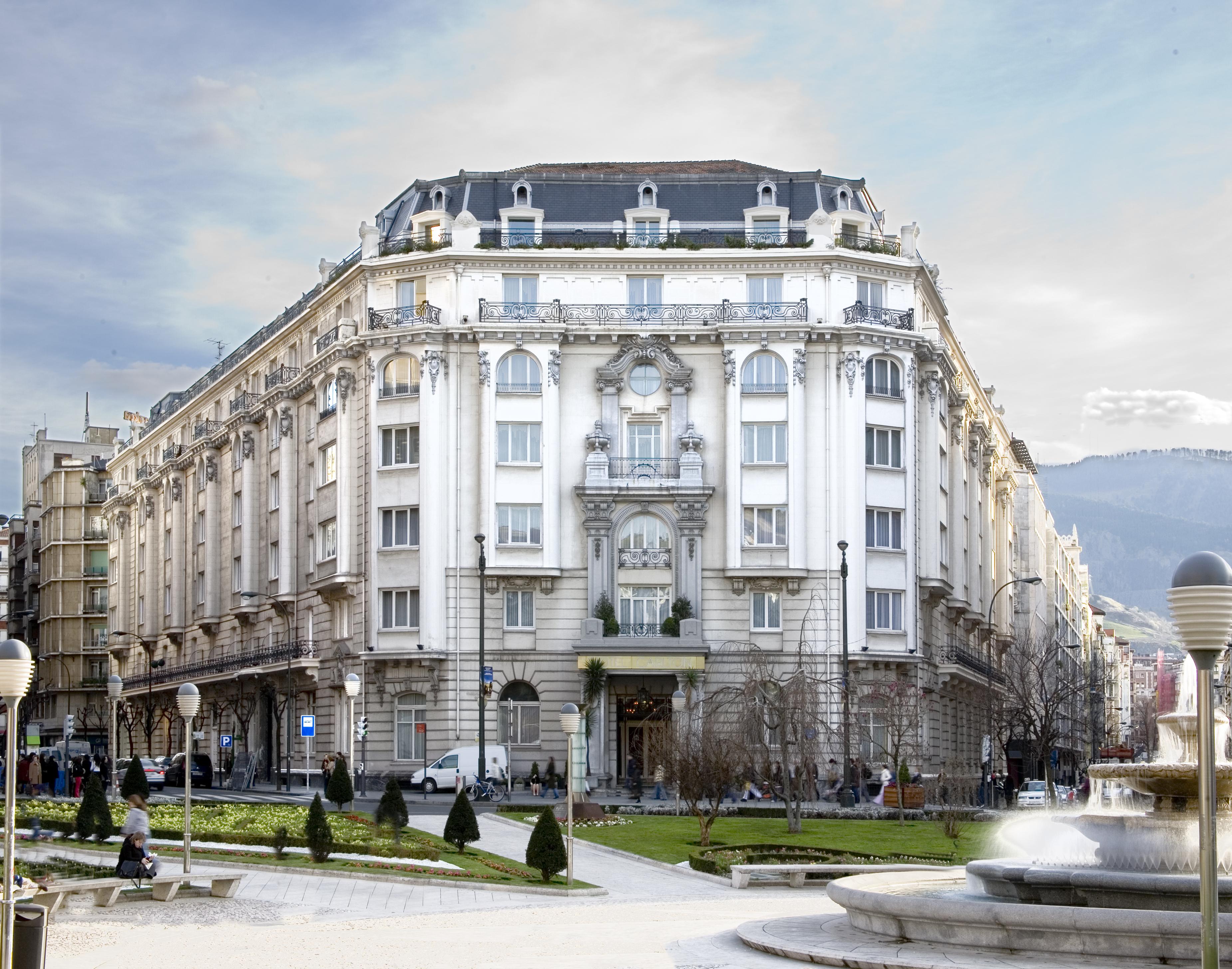 卡尔顿酒店 毕尔巴鄂 外观 照片 The photo shows a grand, historical building with an ornate facade. The architecture features decorative elements, large windows, and a prominent entrance. Surrounding the building is a green area with well-maintained grass and small trees, creating 